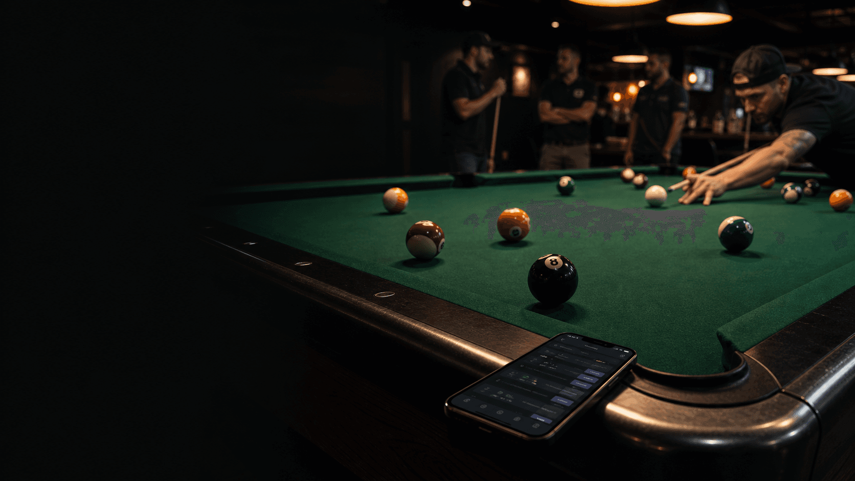 Pool table during league night with a mobile league app resting on the rail.